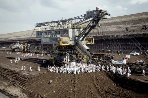 Hundreds of people in white jumpsuits surround a massive machine in a mine. Photo.